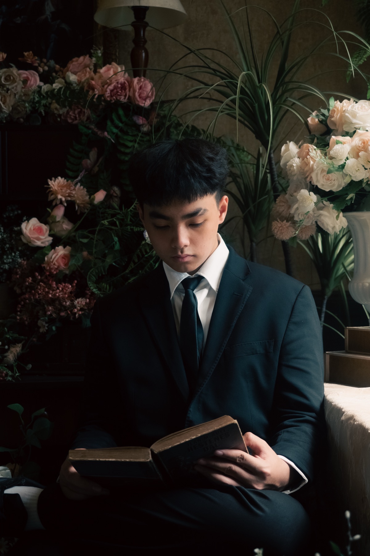 Khang reading a book in a dark suit by a window